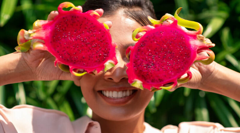 Mulher segurando duas metades de pitaya vermelha em frente ao rosto