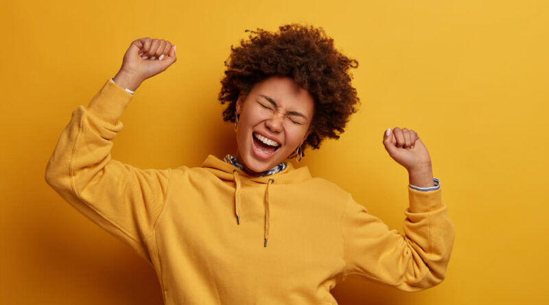 mulher afro-americana com os braços para o alto e sorrindo demonstrando felicidade