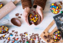 duas mãos segurando um ovo de chocolate com vários chocolates ao redor