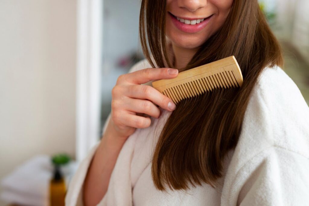 Mulher penteando o cabelo liso e brilhante com pente de madeira durante rotina de cuidados capilares
