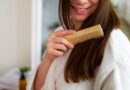 Como deixar o cabelo mais liso naturalmente (sem química) Mulher penteando o cabelo liso e brilhante com pente de madeira durante rotina de cuidados capilares