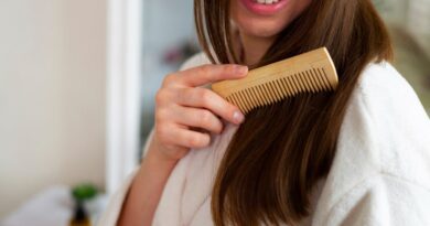 Como deixar o cabelo mais liso naturalmente (sem química) Mulher penteando o cabelo liso e brilhante com pente de madeira durante rotina de cuidados capilares
