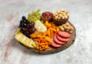 Tábua de petiscos com frutas, queijos, castanhas, salgadinhos e embutidos, representando a tendência girl dinner.