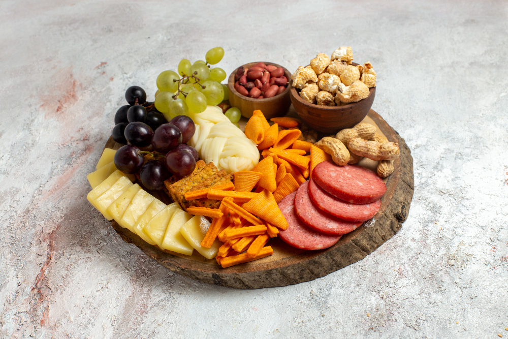 Tábua de petiscos com frutas, queijos, castanhas, salgadinhos e embutidos, representando a tendência girl dinner.