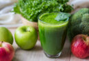Copo de suco verde com maçãs, folhas e vegetais ao redor, representando a tendência de detox do fígado