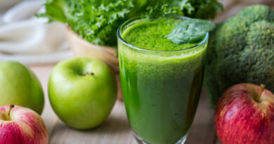 Copo de suco verde com maçãs, folhas e vegetais ao redor, representando a tendência de detox do fígado