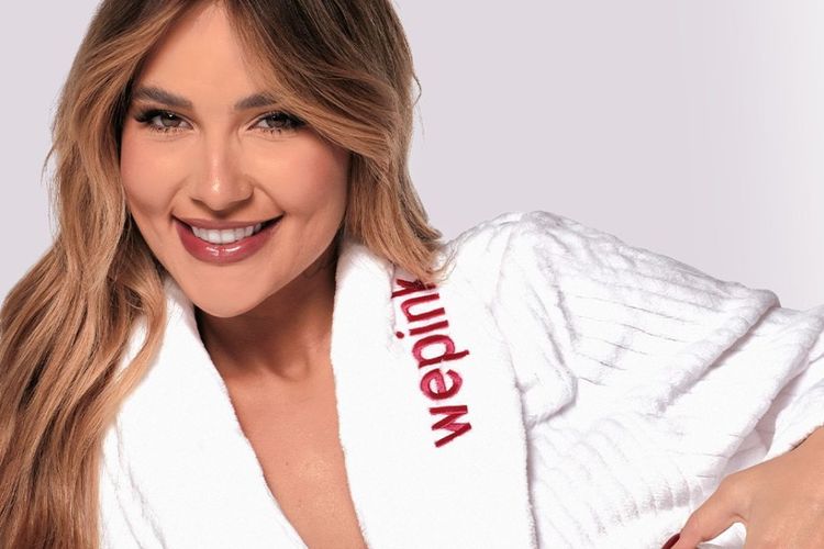 Mulher sorrindo usando roupão branco com logo da WePink