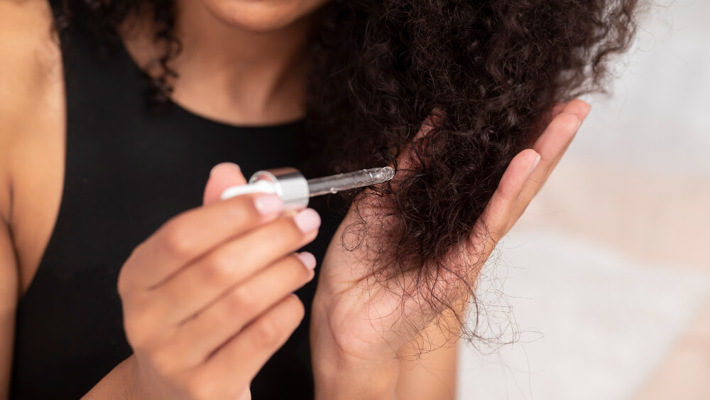 Pessoa aplicando sérum em cabelo cacheado com frizz para ajudar no alinhamento dos fios