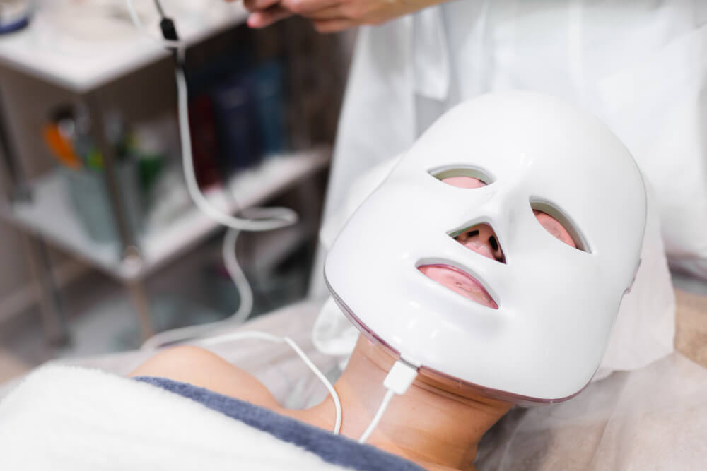 Pessoa usando máscara LED facial durante tratamento de skincare em clínica estética