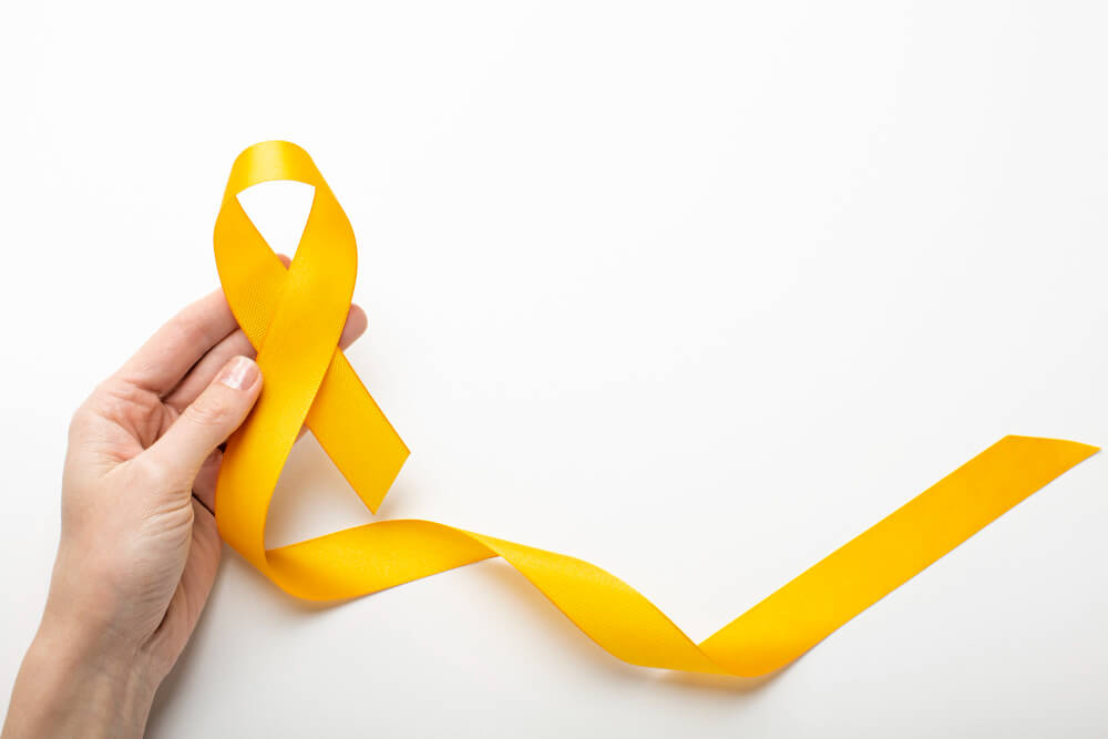 Mão segurando fita amarela, símbolo do Julho Amarelo e da conscientização sobre hepatite B e C