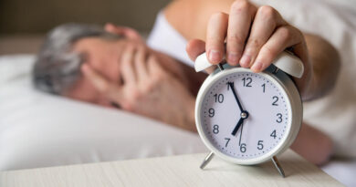 Pessoa acordando cansada e segurando despertador ao lado da cama, representando baixa qualidade do sono
