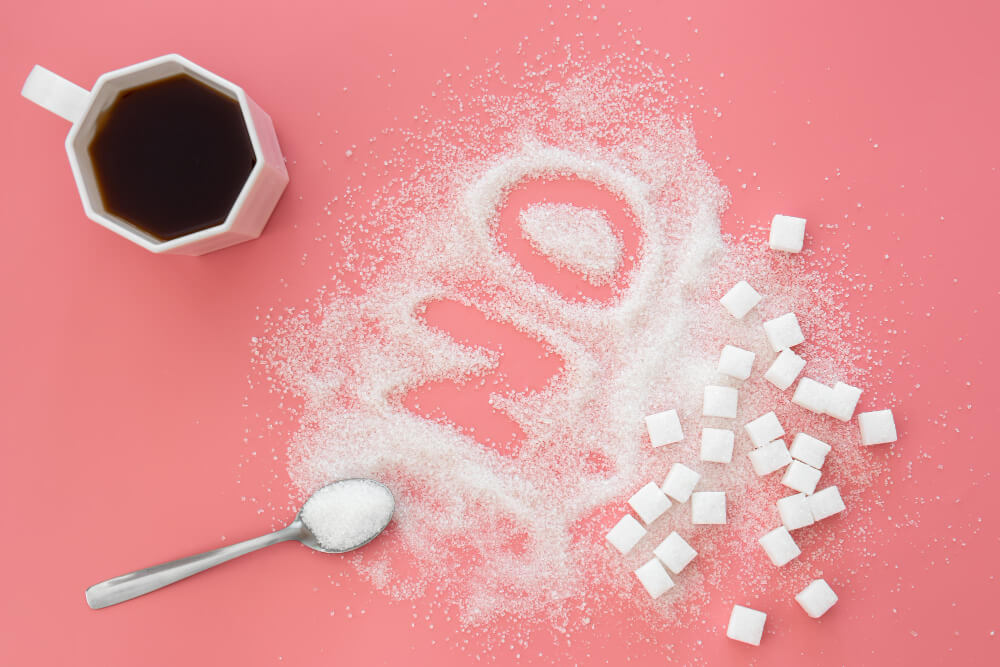 Açúcar espalhado formando a palavra "não" ao lado de xícara de café, representando a redução do açúcar na alimentação