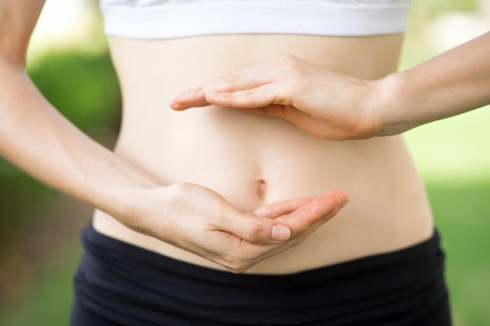 Mulher forma um coração com as mãos sobre a barriga, em referência ao cuidado com a saúde intestinal
