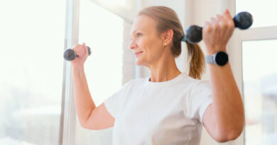 Cuidados hormonais e longevidade: a nova onda que chegou aos 40+ Mulher na casa dos 40 sorrindo enquanto faz treino de força com halteres em ambiente iluminado por luz natural