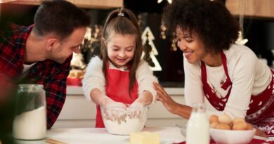 Ceia de Natal: 10 pratos fáceis para montar uma mesa bonita sem gastar muito Família cozinhando junta em cozinha decorada para a ceia de Natal, com uma menina misturando farinha em uma tigela