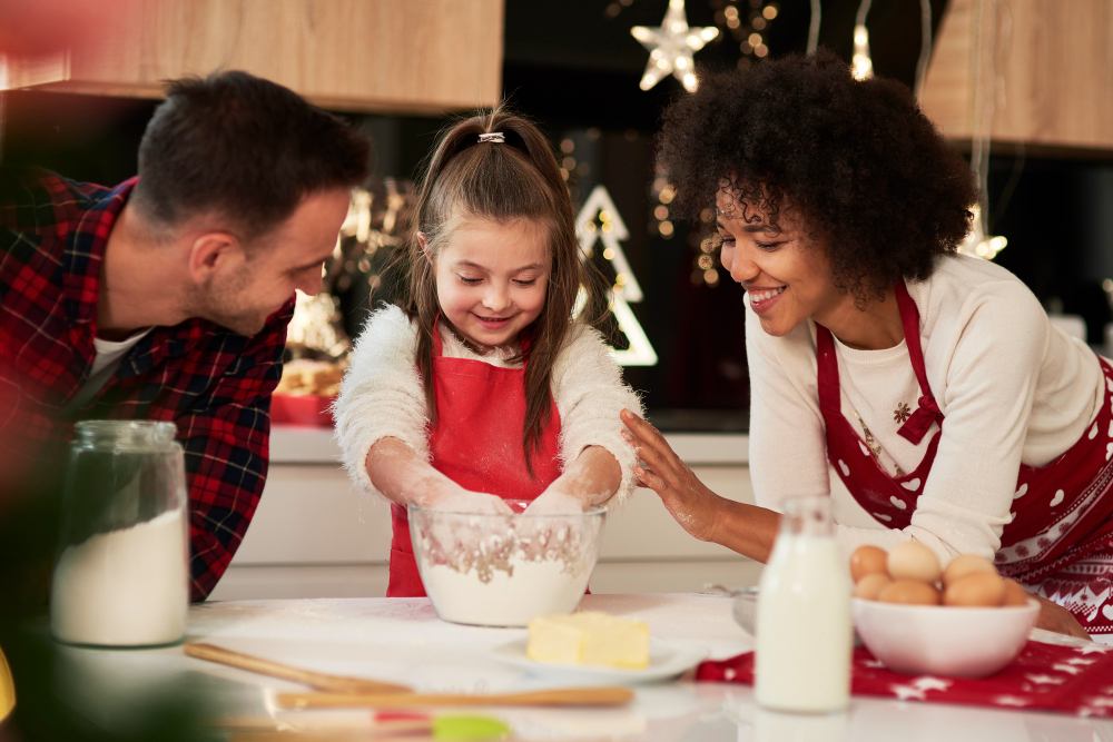 Família cozinhando junta em cozinha decorada para a ceia de Natal, com uma menina misturando farinha em uma tigela