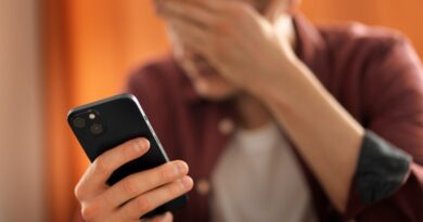 Tempo de tela: você passa horas demais no celular? Faça o teste Pessoa segurando um celular enquanto cobre o rosto com a mão, em ambiente com iluminação alaranjada.